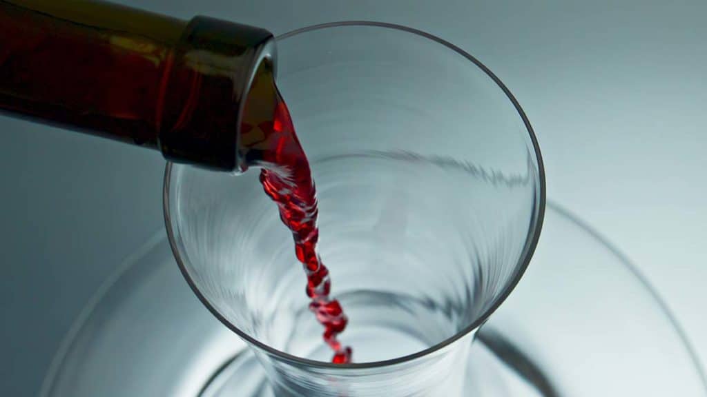 Closeup pouring wine into a decanter bottleneck